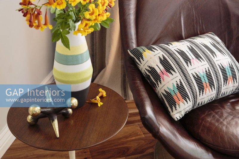 A  leather armchair is accentuated with a colorful pillow with a geometric pattern.