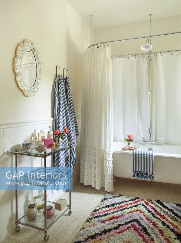 Striped towels and zigzag rainbow rug add zip to an all-white bath.  In a neutral space like this, itâ€™s easy to dramatically change out the look of the room simply by playing with the accessories. 
