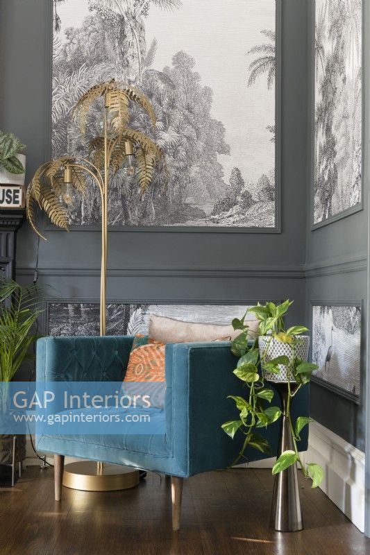 Gold fern floor lamp and a teal upholstered chair in the corner of a grey painted living room with paneling filled with monochrome tropical tree wallpaper