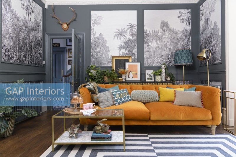 Orange velvet sofa in a grey living room with panels infilled with monochrome tropical tree patterned wallpaper