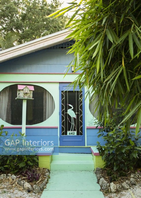 The front porch of the brightly colored cottage features unusual oval screened window openings. 