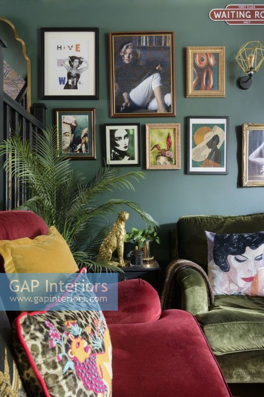 Salon style gallery wall in a green living room with red and green velvet sofas.