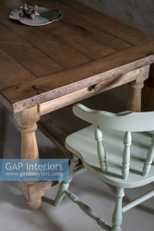 Detail of wooden dining table and pale blue painted chair