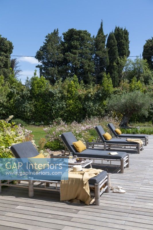 Grey and yellow cushions on recliners on decking in country garden 