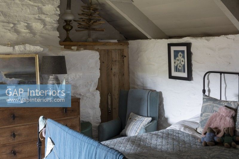 Cosy bedroom in rustic cottage, whitewashed walls and beams, and metal framed bed covered with comfortable blue cover