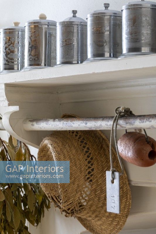 Kitchen shelving detail, with straw, hat, and metal storage containers