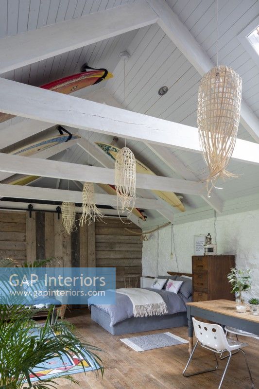 Converted barn, with bed, furniture, and desk. Wooden beams and rustic decoration, surfboards decorating the wooden roof