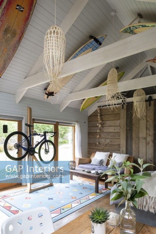 Converted barn, with bed, furniture, and bike stand. Wooden beams and rustic decoration, surfboards decorating the wooden roof