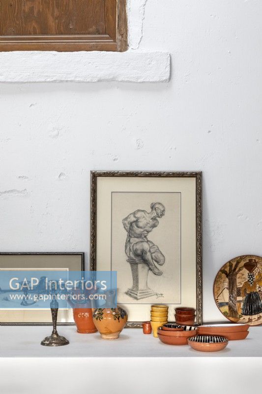 Detail of ceramics and framed paintings on white wall shelf