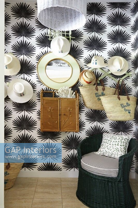 A tropical hat room with black and white palmetto wall paper and vintage wicker furnishings.