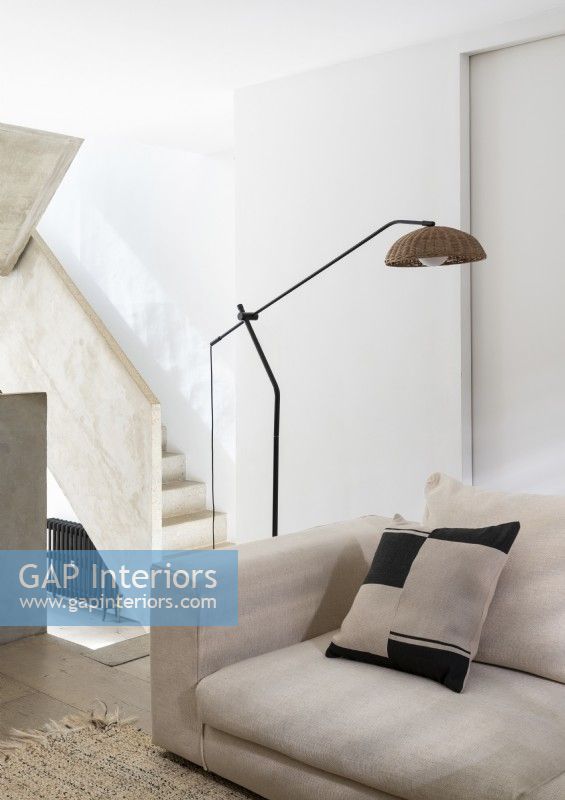 Floor lamp over cream sofa with concrete staircase in background
