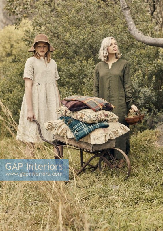 Two women in garden with cushions on antique wheelbarrow