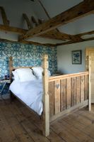 Boonshill Farm, East Sussex. Interior of bedroom with reclaimed wooden bed by mick shaw from old staircase and floorboards. peacock blue wallpaper decorates wall. 