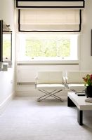 Modern white living room with armchairs and window with cream roman blind