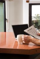 Man Reading Newspaper with Laptop and Coffee