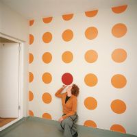 A woman laying against a white wall with yellow polka dots