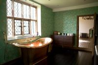 Copper bath next to lead paned window in traditional bathroom