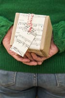 Woman hiding christmas present wrapped with music sheet paper