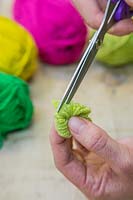 Making christmas pompom decorations - Carefully push the scissor blade into the bundle of wool and cut the strands of wool in half 