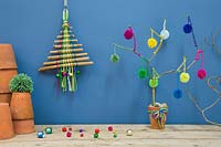 A colourful christmas tree made with sticks, coloured wool and miniature baubles against a blue backdrop
