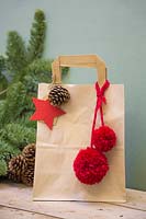 Brown paper christmas gift bag decorated with pine cone, felt star and wool pompoms