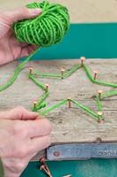 Making a christmas star decoration - Weave the green wool between the copper nails to recreate the star shape