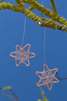 Making copper wire stars - finished decorations hanging from a lichen covered branch against a blue background