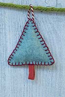 Making stitched felt christmas decorations - miniature christmas tree made from felt and decorative string, hanging against a wooden panel