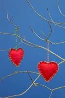 Red hearts stitched together with felt fabric, hanging from  twigs