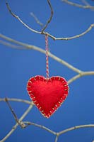 Red heart stitched together with felt fabric, hanging from  twig