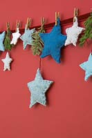 A variety of coloured felt stars hanging against a red background 