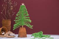 Christmas tree made from green wool mounted in an upturned terracotta pot, against a burgundy background 