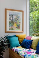 Framed painting over window seat with colourful cushions 