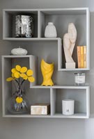 Display of ornaments on geometric shelf on grey painted wall 