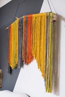 Display of colourful threads hanging on part painted wall