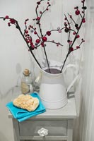 Enamel jug with stems of rosehip on bathroom cabinet 