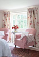 Gingham covered armchairs and floral curtains in country bedroom 