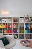 Large bookcases with books arranged by colour and neon art 