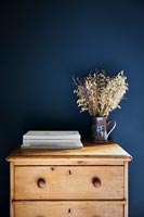 Pine chest of drawers next to dark blue painted wall 