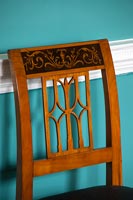 Antique cherry wood dining chair next to dado rail on painted wall 