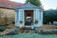 Lit fire pit outside wooden summer house in country garden - December 