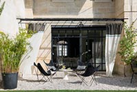 Garden chairs and table on gravel terrace with curtains for shade 