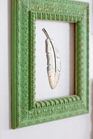 Green painted wooden picture frame on wall with carved feather