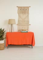 Orange blanket over sideboard with macrame wall hanging 