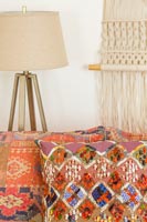 Patterned orange cushions with lamp and macrame wall hanging behind 