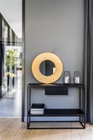 Console table with circular gold mirror against grey painted wall 