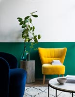 Modern living room with green half painted feature wall behind yellow chair  