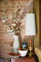 White enamel vase filled with branches of blossom on side table 