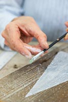 Close up detail of woman using a paint brush to flick paint onto wood to simulate snow falling