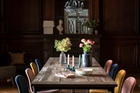 Different coloured chairs around wooden dining table 